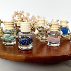 May include: A collection of small glass bottles with cork tops and colorful stones inside. The bottles are hanging from a string and are arranged on a wooden surface.