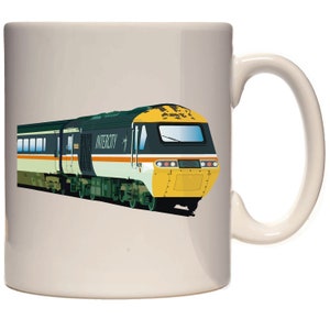 Könnte beinhalten: Eine weiße Keramiktasse mit einer Illustration eines grün-gelben Intercity-Zuges. Der Zug hat eine gelbe Front und einen schwarz-grünen Körper mit dem Wort "Intercity" auf der Seite.
