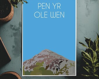 May include: A framed art print featuring a mountain illustration with a blue sky background. The text "PEN YR OLE WEN" is displayed in white. The mountain is depicted in shades of brown, green, and gray.