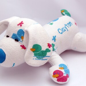 May include: White plush dog toy with blue, green, and pink duck designs and the name "Clayton" embroidered on the back.