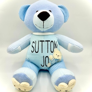 May include: A light blue plush teddy bear featuring a white muzzle, dark brown nose, and ears with a blue and white gingham pattern. The chest is embroidered with the name SUTTON JO and includes a small applique of a cream-colored bear.