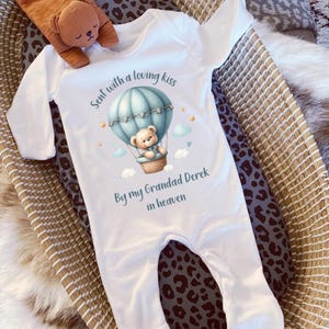 May include: White baby onesie with a blue hot air balloon and a teddy bear. The text on the onesie reads "Sent with a loving kiss by my Grandad Derek in heaven."