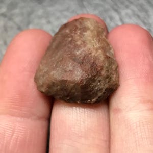 May include: A small, rough, brown and gray rock with a slightly pointed shape.