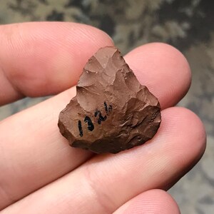 May include: A brown, triangular-shaped arrowhead with a black inscription that reads "1324".