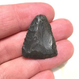 May include: A dark gray triangular arrowhead with a smooth, polished surface.