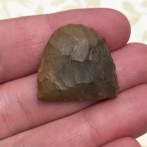 May include: A brown, arrowhead-shaped stone tool with a rough, textured surface.