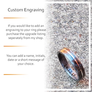 Op de afbeelding: Een ring met een donkere, getextureerde band en een lichtere binnenkant, met de datum 14.12.17 gegraveerd. De afbeelding bevat ook tekst over aangepaste graveeropties voor ringen.