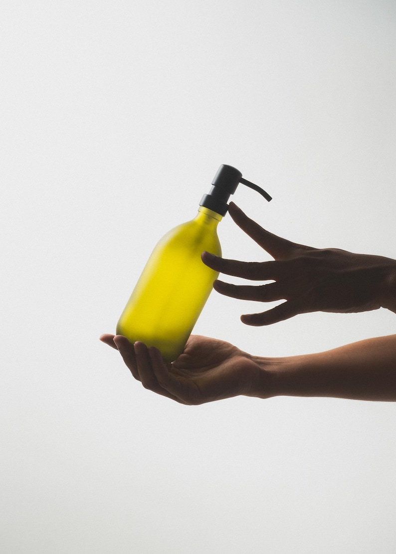 May include: A person's hands holding a yellow glass bottle with a black pump dispenser.