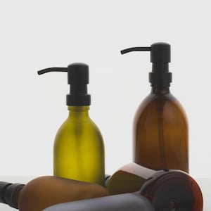 May include: Four glass bottles with black pump tops. Two bottles are amber coloured, one is green, and one is brown. The bottles are on a white surface.