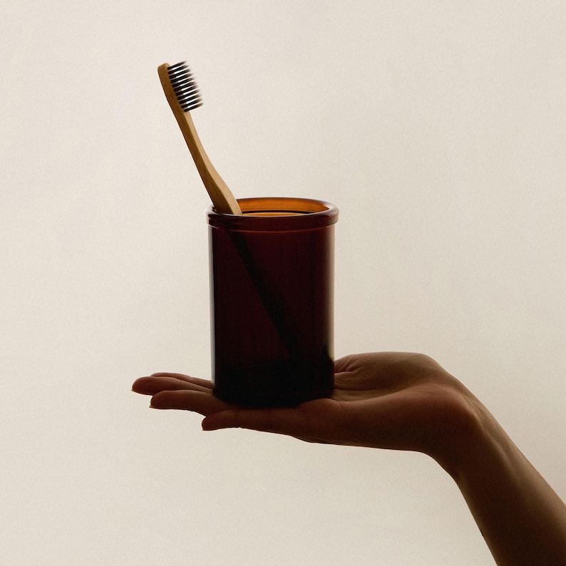 Puede incluir: Un portacepillos de vidrio marr&oacute;n con un cepillo de dientes de madera en su interior.