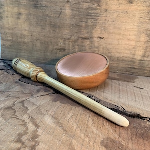May include: A wooden mortar and pestle set with a copper-colored interior bowl. The pestle is light-colored wood with a rounded end. The bowl is oval-shaped and sits next to the pestle on a wooden surface.