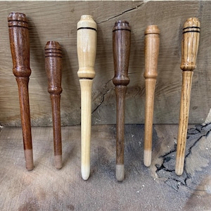 May include: Six wooden tools in shades of brown and beige. Each tool has a handle and a rounded top. The tips of the tools are a lighter colour than the rest. The tools are arranged vertically.