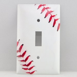 May include: White light switch cover with a baseball graphic. The baseball is white with red stitching.