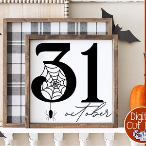 Pode incluir: Uma placa preta e branca com o n&uacute;mero 31 em fonte grande, com uma teia de aranha dentro do 3. O texto "Outubro" est&aacute; escrito em it&aacute;lico abaixo dos n&uacute;meros. A placa est&aacute; emoldurada em uma moldura de madeira r&uacute;stica.