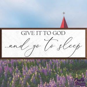 May include: A wooden sign with the text "Give it to God...and go to sleep" in black script font. The sign is brown with a white background and is sitting on a bed of purple lupine flowers.