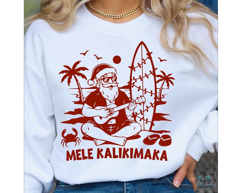 May include: White sweatshirt with a red graphic of Santa Claus playing a ukulele on a beach, with a surfboard, palm trees, and the words "MELE KALIKIMAKA". The design includes a crab, birds, and sandals.