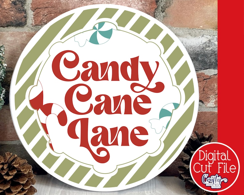 Op de afbeelding: Een rond, wit bord met een groene en witte gestreepte rand. Het bord zegt "Candy Cane Lane" in rode letters met een retro-lettertype. Het bord is versierd met snoepstokken en pepermuntjes.