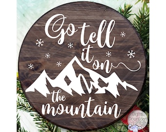 Puede incluir: Un letrero redondo de madera con el texto "Go tell it on the mountain" en letras blancas. El letrero está decorado con copos de nieve y una silueta blanca de una cordillera.