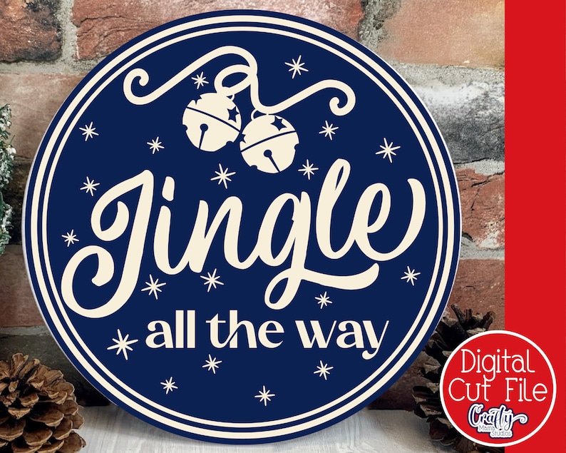 Op de afbeelding: Een rond blauw en wit bord met de tekst "Jingle all the way" in een wit cursief lettertype. Het bord is versierd met witte sneeuwvlokken en twee witte bellen.