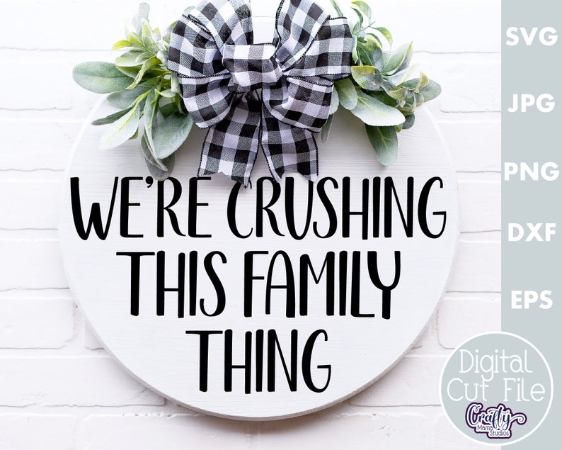 K&ouml;nnte beinhalten: Ein wei&szlig;es rundes Schild mit schwarzem Text, der "We're crushing this family thing" lautet. Das Schild ist mit einer schwarz-wei&szlig;en karierten Schleife und Gr&uuml;npflanzen verziert.
