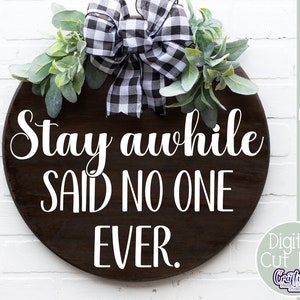 K&ouml;nnte beinhalten: Ein rundes Holzschild mit einer schwarz-wei&szlig;en karierten Schleife und Gr&uuml;n. Das Schild sagt "Stay awhile SAID NO ONE EVER."