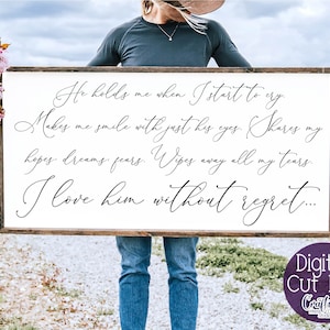 May include: A white wooden sign with black calligraphy text that reads "He holds me when I start to cry. Makes me smile with just his eyes. Shares my hopes, dreams, fears. Wipes away all my tears. I love him without regret..."