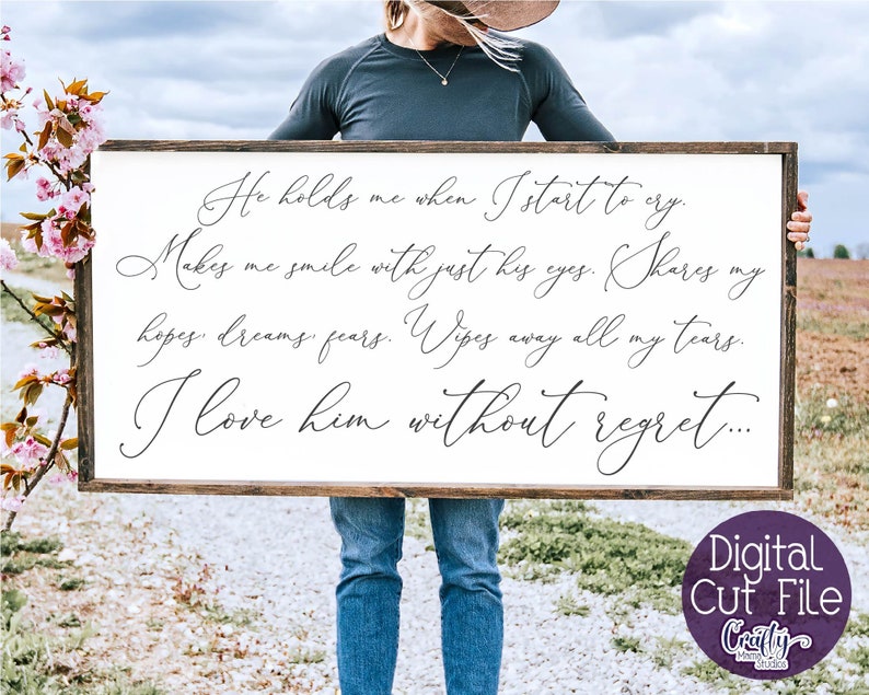 May include: A white wooden sign with black calligraphy text that reads "He holds me when I start to cry. Makes me smile with just his eyes. Shares my hopes, dreams, fears. Wipes away all my tears. I love him without regret..."