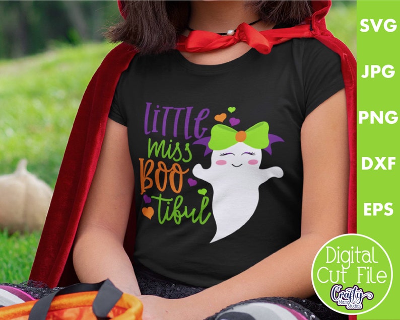 May include: A black t-shirt with a cute ghost graphic and the text "Little Miss Boo-tiful". The ghost has green and purple hair and a pink bow. The shirt is worn by a child wearing a red cape.