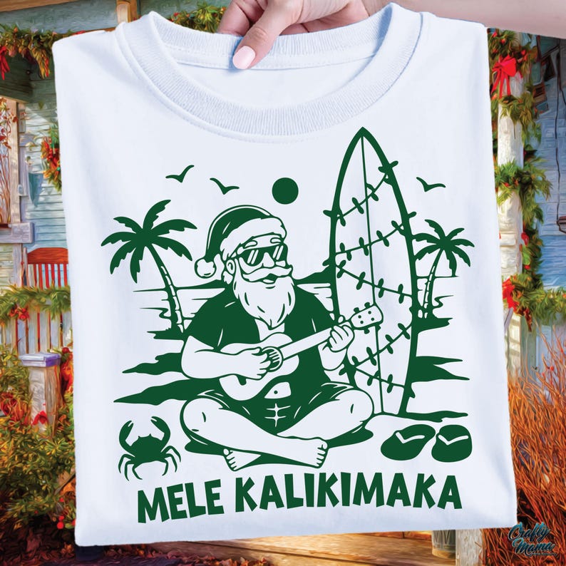 May include: White t-shirt with a green graphic of Santa Claus playing a ukulele on a beach, with a surfboard, palm trees, and the text "MELE KALIKIMAKA." The design includes a crab and flip-flops, evoking a tropical Christmas theme.