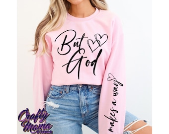May include: Pink sweatshirt with the text "But God makes a way" in black script with two small hearts above the word "God" and a larger heart on the sleeve.