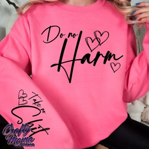 以下が含まれることがあります： ピンクのトレーナーに、黒い筆記体で「Do no Harm」という文字と、小さなハートが3つ描かれています。左袖には、黒い筆記体で「Take no Shit」という文字と、小さなハートが3つ描かれています。