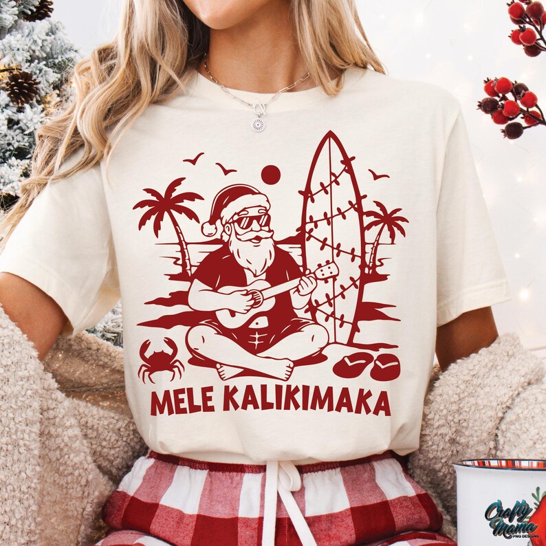 May include: Cream-colored t-shirt with a red graphic of Santa Claus playing a ukulele on a beach, with palm trees, a surfboard, and the text "MELE KALIKIMAKA".