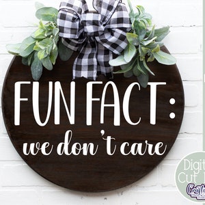 K&ouml;nnte beinhalten: Ein rundes Holzschild mit einer schwarz-wei&szlig;en karierten Schleife und Gr&uuml;n. Das Schild sagt "FUN FACT: we don't care".