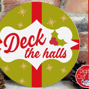 Op de afbeelding: Een rond, groen en rood kerstbord met de tekst "Deck the halls" in een witte banner met een rode hulsttak.