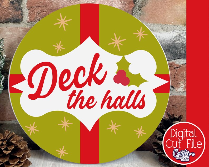 Op de afbeelding: Een rond, groen en rood kerstbord met de tekst "Deck the halls" in een witte banner met een rode hulsttak.