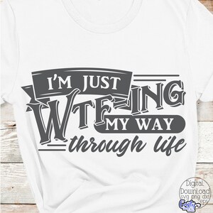 May include: White t-shirt with a dark gray graphic that reads "I'M JUST WTFING MY WAY THROUGH LIFE." The text is in a bold, stylized font. The shirt is made of a soft material.