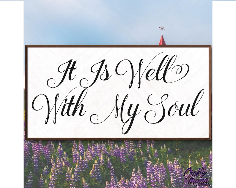 May include: A wooden sign with the text "It Is Well With My Soul" in a decorative script font. The sign is framed in brown and has a white background. The sign is displayed in front of a field of purple lupine flowers.