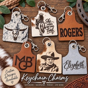 May include: Six livestock ear tag-shaped keychains with metal lobster clasps. Designs include a cow skull, a person on horseback with the text 'She rides her own trail', the name 'ROGERS', the initials 'MGB+', a cowboy portrait, and the name 'Elizabeth'.