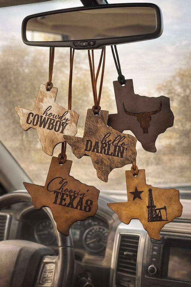 May include: Five Texas-shaped hanging ornaments made of leather and faux fur, featuring brown and tan textures. The ornaments display the text 'howdy COWBOY', 'hello DARLIN', 'Choosin' TEXAS', a longhorn skull graphic, and a star with an oil derrick.