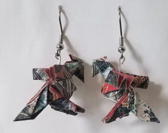 May include: A pair of origami earrings featuring a colorful, multi-patterned design. The earrings are made of paper and have silver hooks.