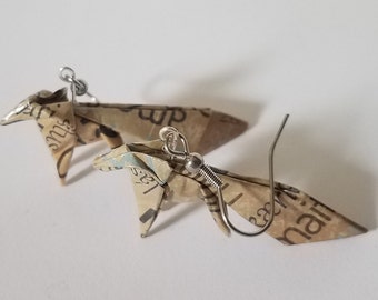Può includere: Un paio di orecchini origami realizzati con carta riciclata, con un design a forma di cavallo. Gli orecchini sono di colore argento e hanno una chiusura a gancio.