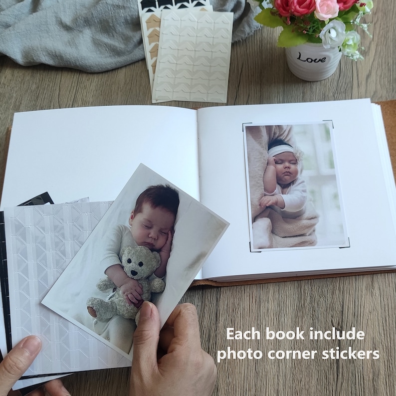 Puede incluir: Un &aacute;lbum de fotos blanco con una cubierta de cuero marr&oacute;n. El &aacute;lbum est&aacute; abierto para revelar dos fotos de beb&eacute;s. Las fotos est&aacute;n decoradas con pegatinas de esquina de fotos blancas. El texto "Each book include photo corner stickers" est&aacute; escrito debajo de las fotos.