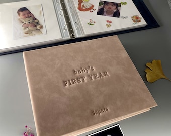 May include: A light brown photo album with the text "baby's FIRST YEAR" embossed on the front cover. The album is closed and the name "Sophia" is embossed on the bottom right corner.