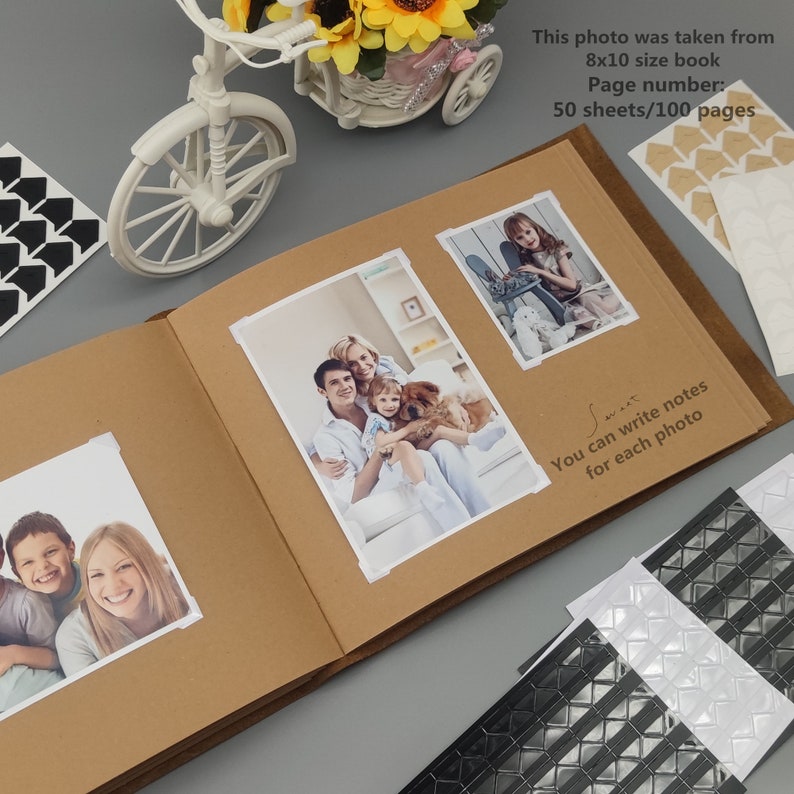 Puede incluir: Un &aacute;lbum de fotos marr&oacute;n con una cubierta de cuero y una bicicleta blanca en la portada. El &aacute;lbum est&aacute; abierto en una p&aacute;gina con dos fotos, una de una familia con un perro y la otra de una ni&ntilde;a. El &aacute;lbum tiene una nota que dice "Puedes escribir notas para cada foto".