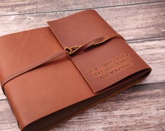 May include: Brown leather photo album with a leather strap and a personalized inscription that reads "Our First Year ♥ Est. April 9, 2022 Rico ♥ Sabrina"