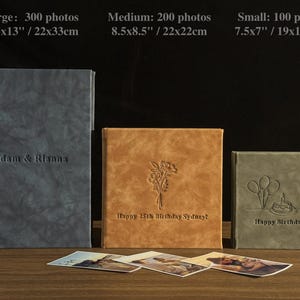 Peut inclure: Trois albums photo personnalis&eacute;s de diff&eacute;rentes tailles : grand (22x33cm), moyen (22x22cm) et petit (19x17.5cm). Les albums sont gris, beige et vert, avec des textes et des motifs en relief. Le grand album dit "Adam & Rianna".