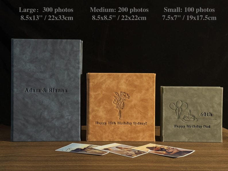 Peut inclure: Trois albums photo personnalis&eacute;s de diff&eacute;rentes tailles : grand (22x33cm), moyen (22x22cm) et petit (19x17.5cm). Les albums sont gris, beige et vert, avec des textes et des motifs en relief. Le grand album dit "Adam & Rianna".