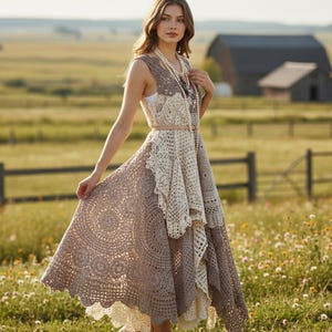 Peut inclure: Robe longue sans manches en crochet, dans les tons marron et crème. La robe présente un motif circulaire détaillé sur la jupe et un design superposé. Une fine ceinture cintre la taille et un long collier de perles ajoute une touche d'élégance. En arrière-plan, un champ avec une grange.