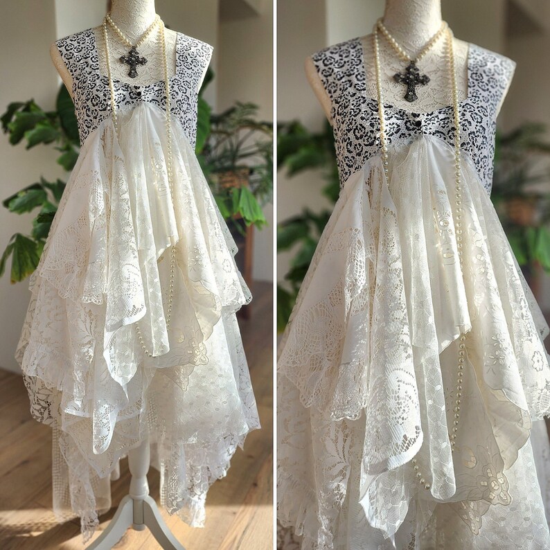 May include: A vintage-style dress displayed on a mannequin. The dress features a black and white patterned bodice, layered white lace skirt, and a pearl necklace with a cross pendant. The dress is a unique, bohemian style.