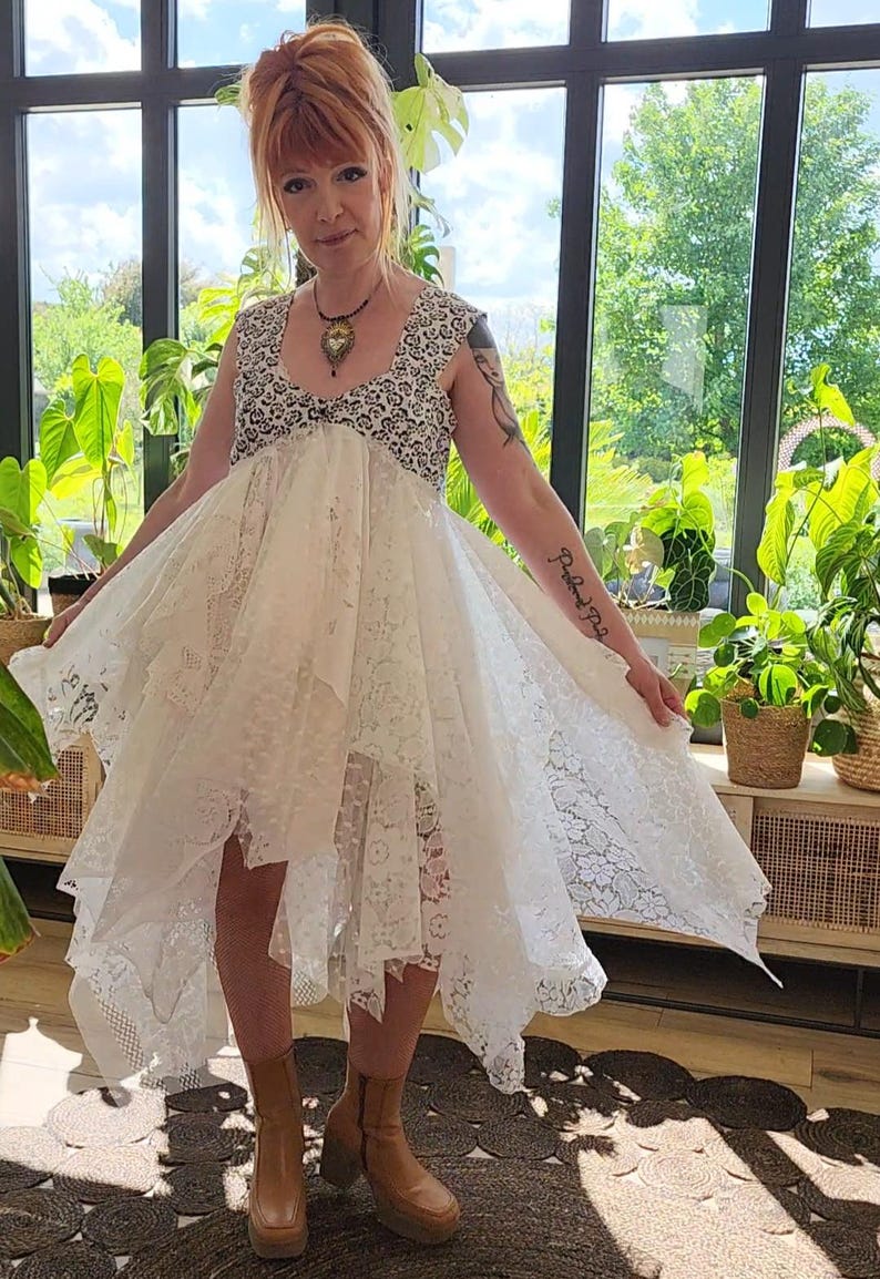 May include: A white lace dress with a high-low hemline and a black and white patterned bodice. The dress is sleeveless and has a flowing, layered skirt. The person is wearing brown platform boots.